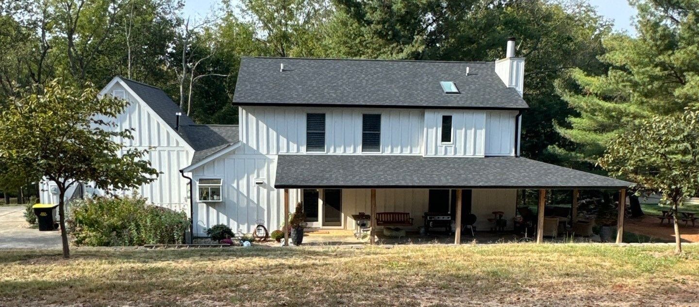 White two-story house with a porch and attached garage in a wooded yard