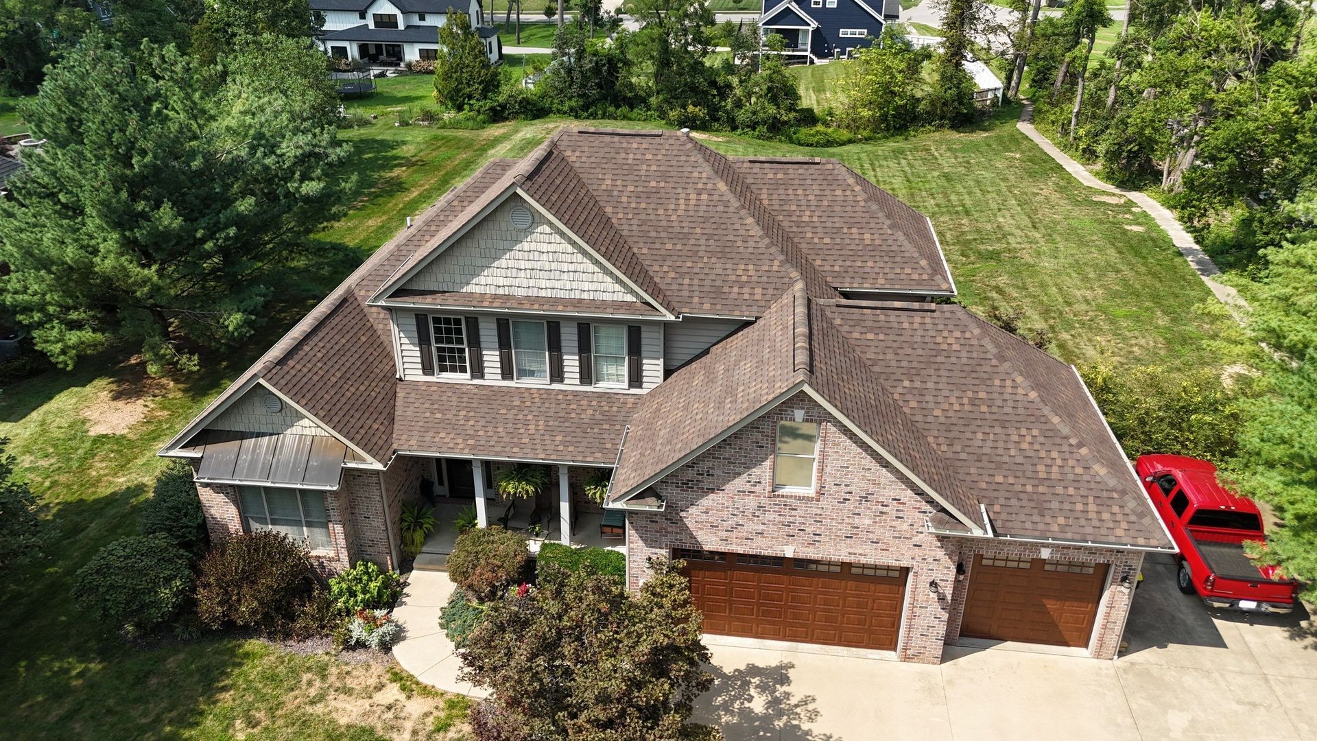 Aerial view of a suburban house with a brown roof, brick garage, and a red truck parked beside it.