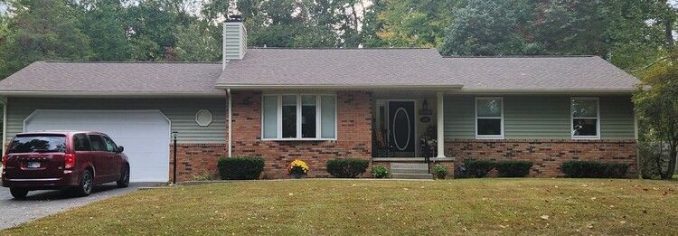 Suburban brick house with gray roof, attached garage, and red SUV parked in the driveway