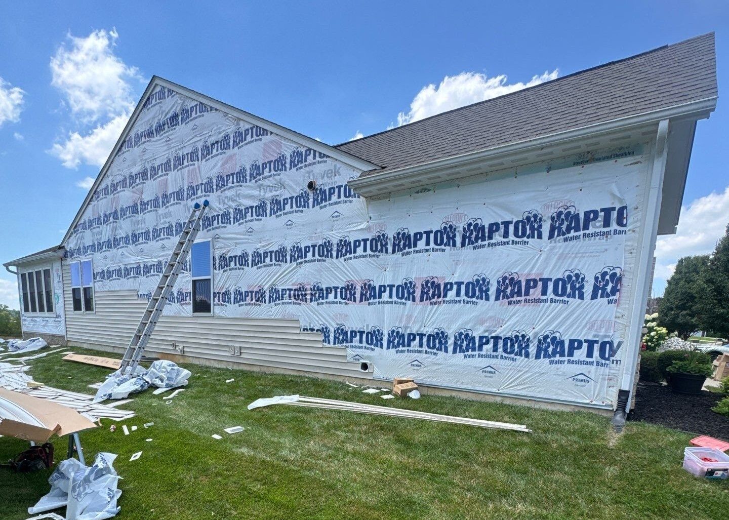 House under construction with white house wrap, blue sky, and grassy yard
