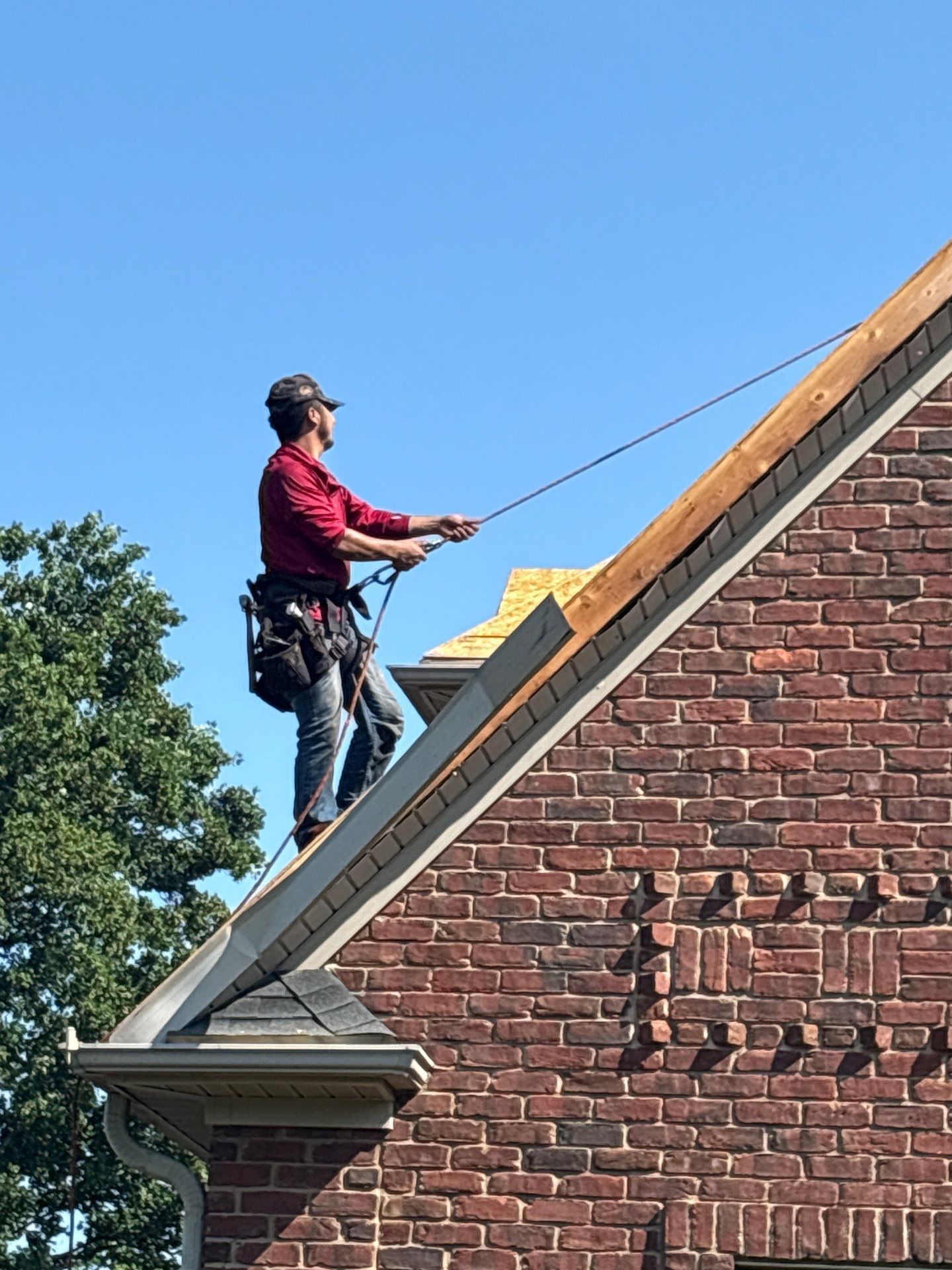 Worker on a steep brick roof securing a rope under a blue sky