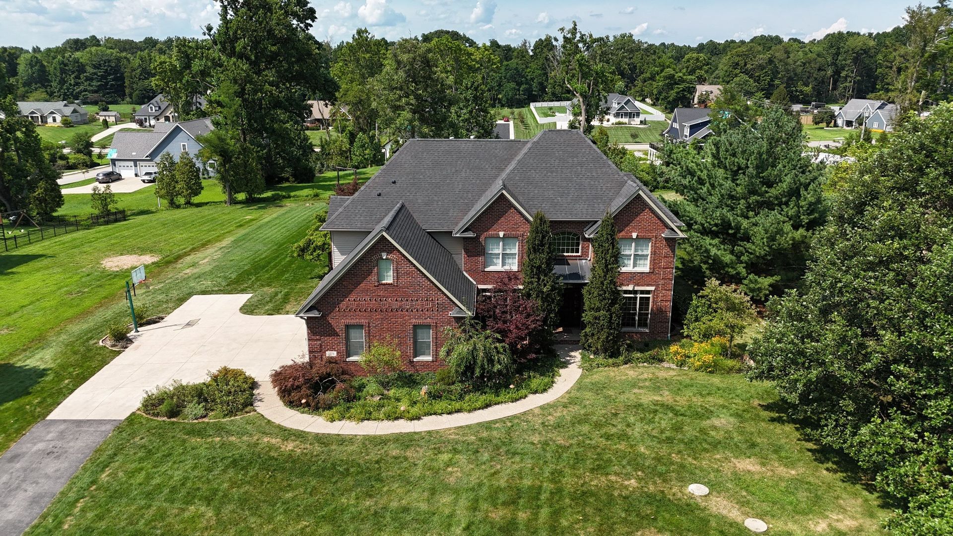 Brick house with gray roof, driveway, and green lawn in a suburban neighborhood