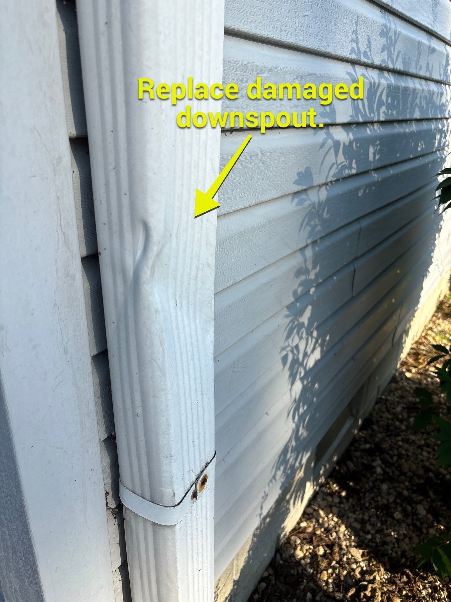 Dented white downspout marked for replacement against vinyl siding