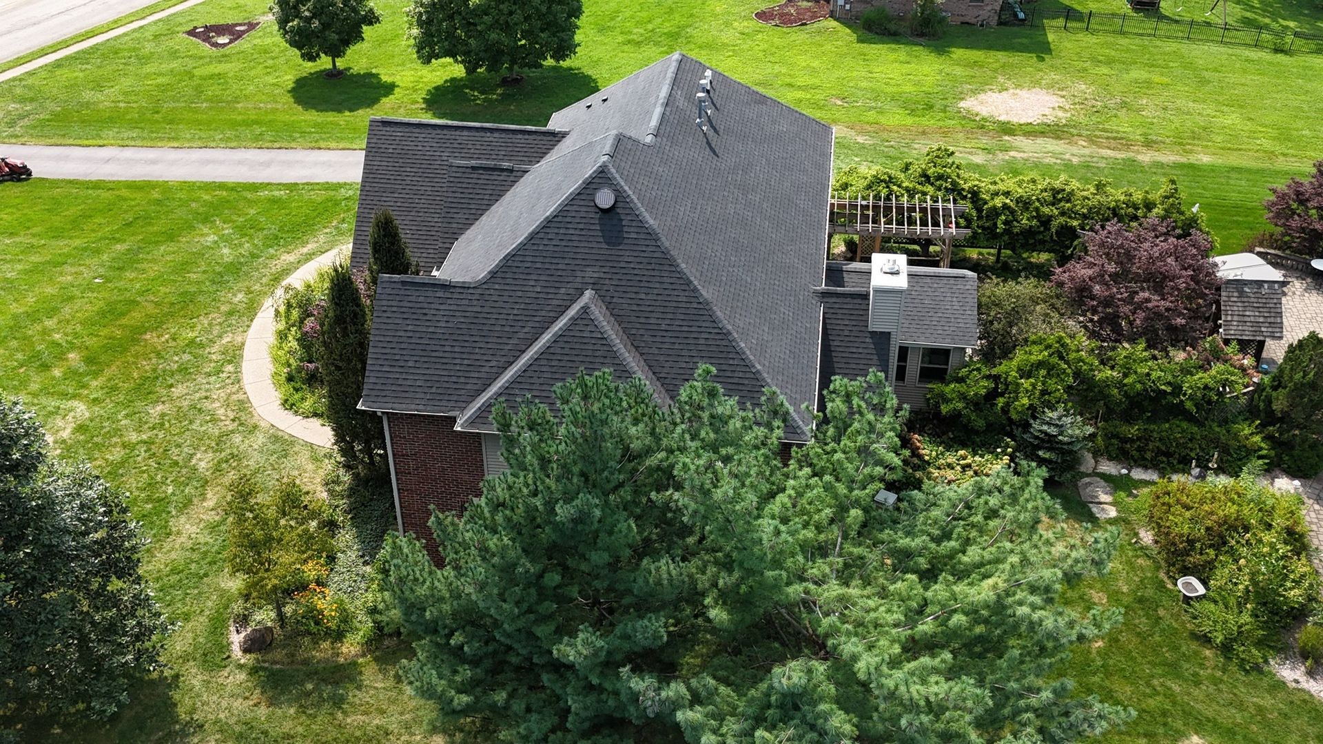 Aerial view of a dark-roofed house surrounded by green lawn and trees