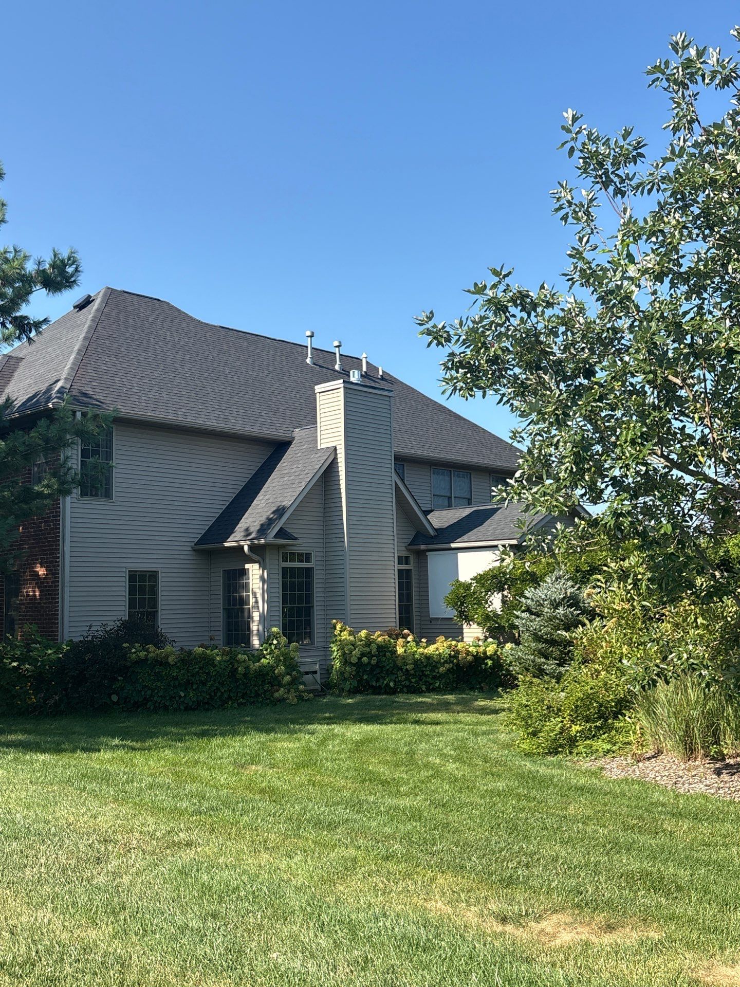 Suburban house with gray roof, white walls, and a green lawn under a clear blue sky