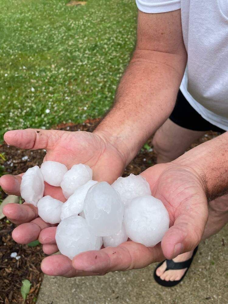 Hands holding large white hailstones outdoors on grass.