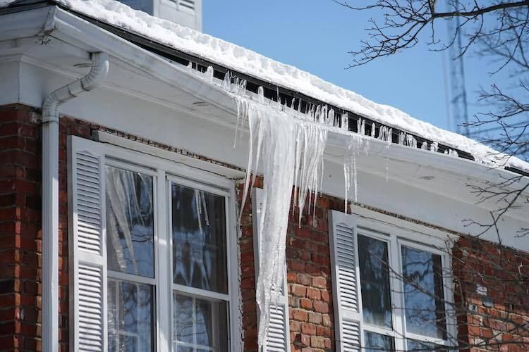 Brick house roof with long icicles hanging over windows on a snowy winter day
