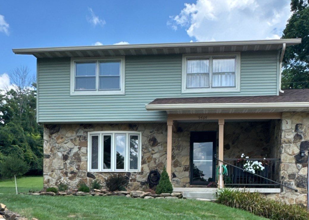 Two-story house with stone lower facade, green siding, and a small front porch under a blue sky