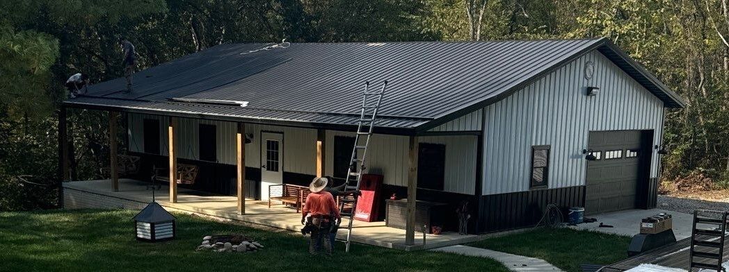White house with a metal roof, front porch, and several people sitting outside in the yard.