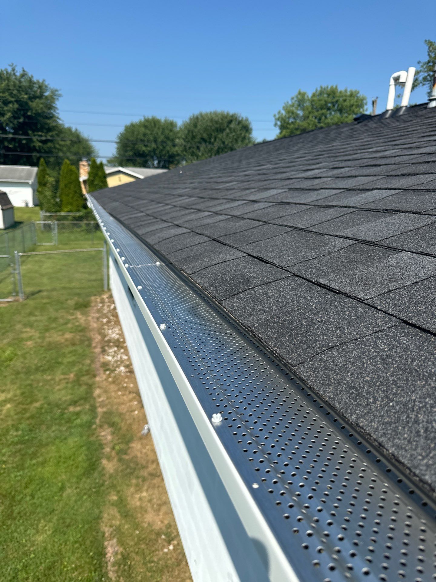 New seamless gutter with perforated guards installed along an asphalt shingle roof