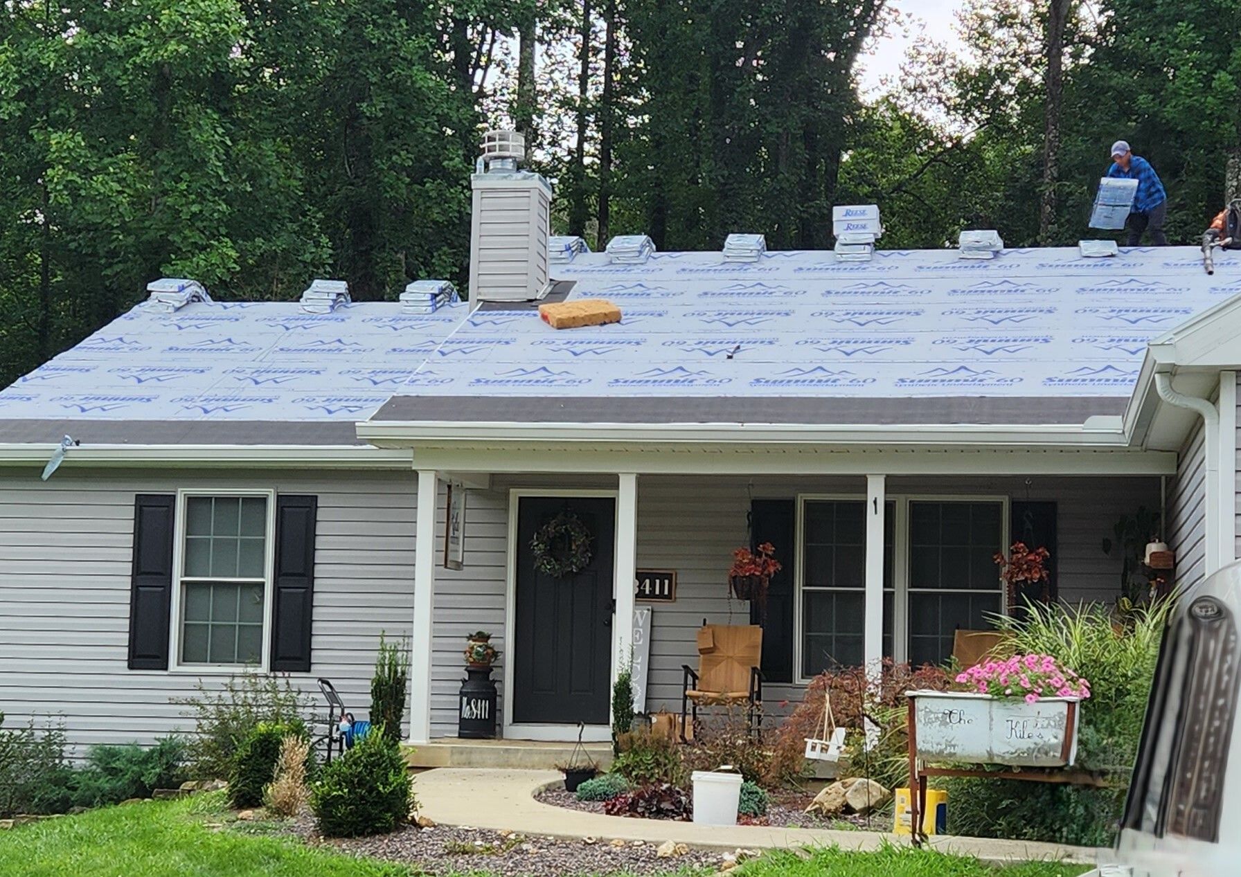 House with new roof under construction, white siding, front porch, and workers on the roof
