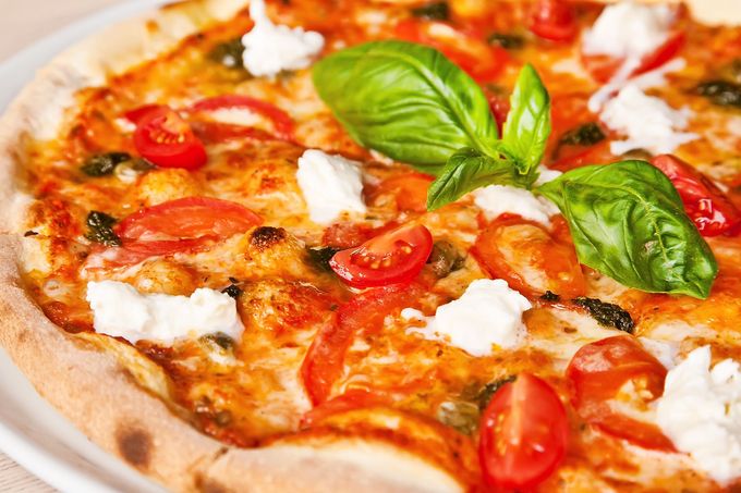 Primo piano di una pizza Margherita con basilico, pomodorini e formaggio fuso su un piatto.