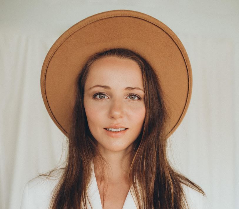 Portrait of a smiling woman wearing a wide-brim tan hat against a light background