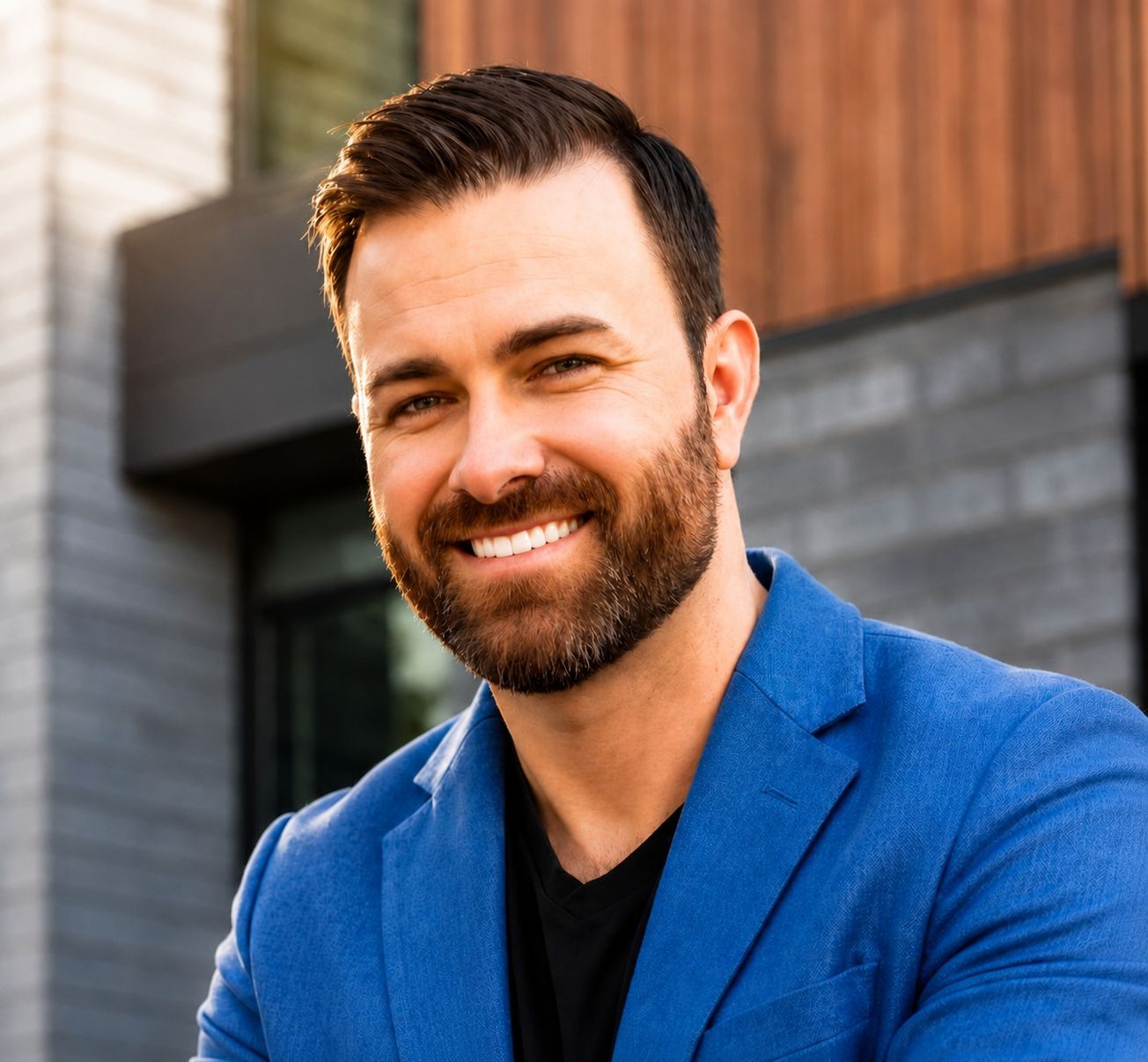 Smiling man in a blue blazer standing outdoors in front of a modern building