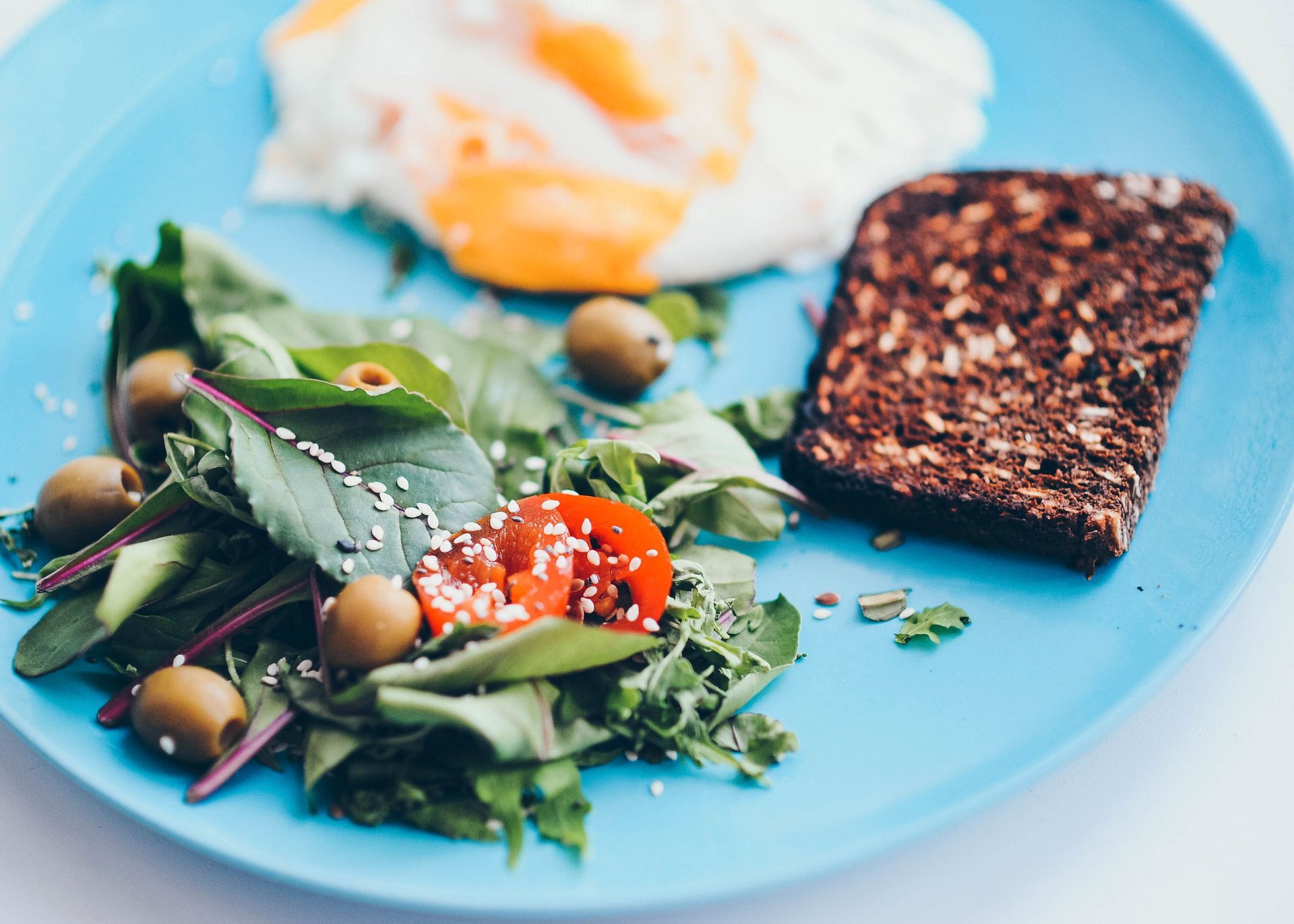 Salad with olives and cherry tomatoes, poached egg, and toasted bread on a blue plate