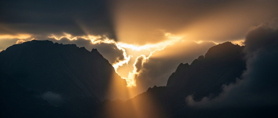 Sunlight beams through dark clouds over a mountain valley at dawn
