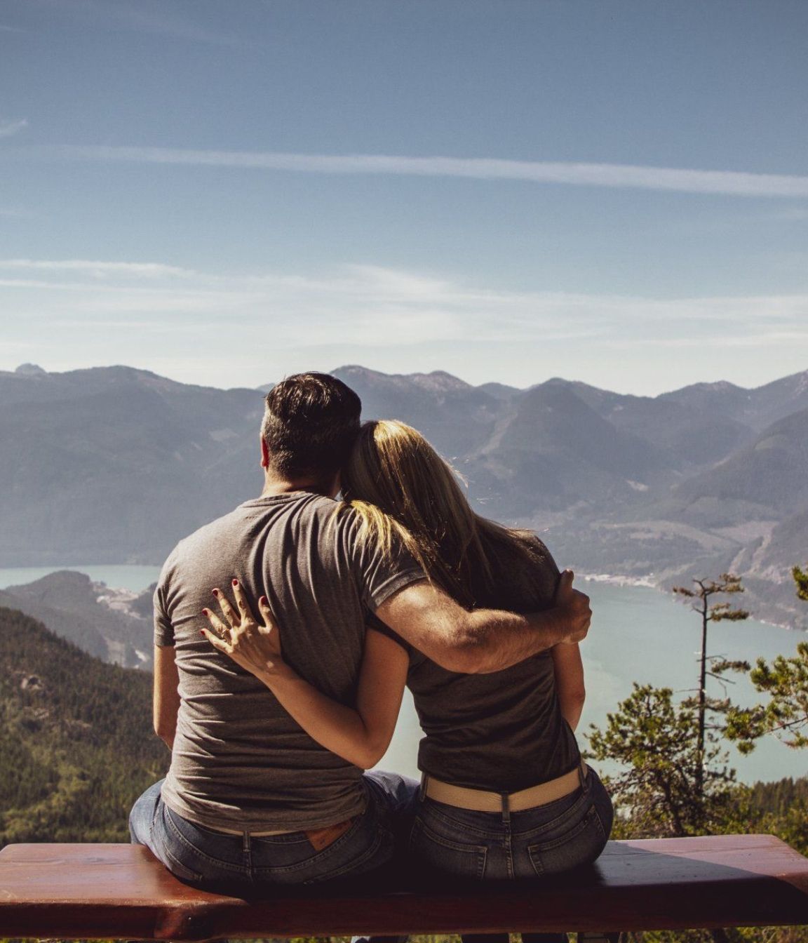 A man and a woman are sitting on a bench looking at the mountains