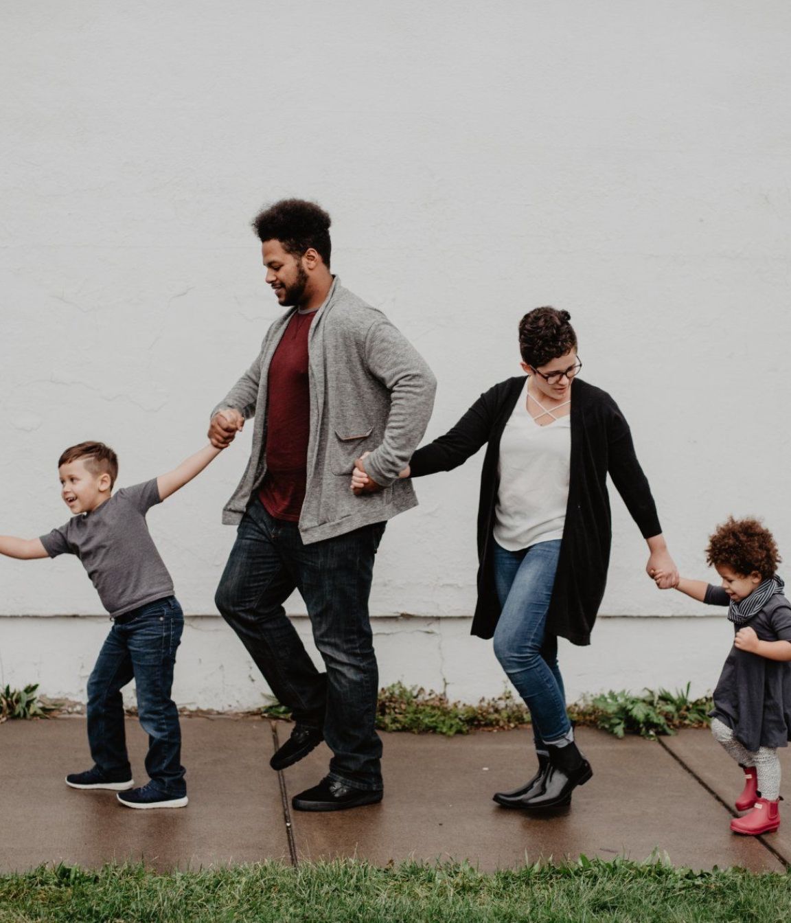 A family is walking down a sidewalk holding hands.