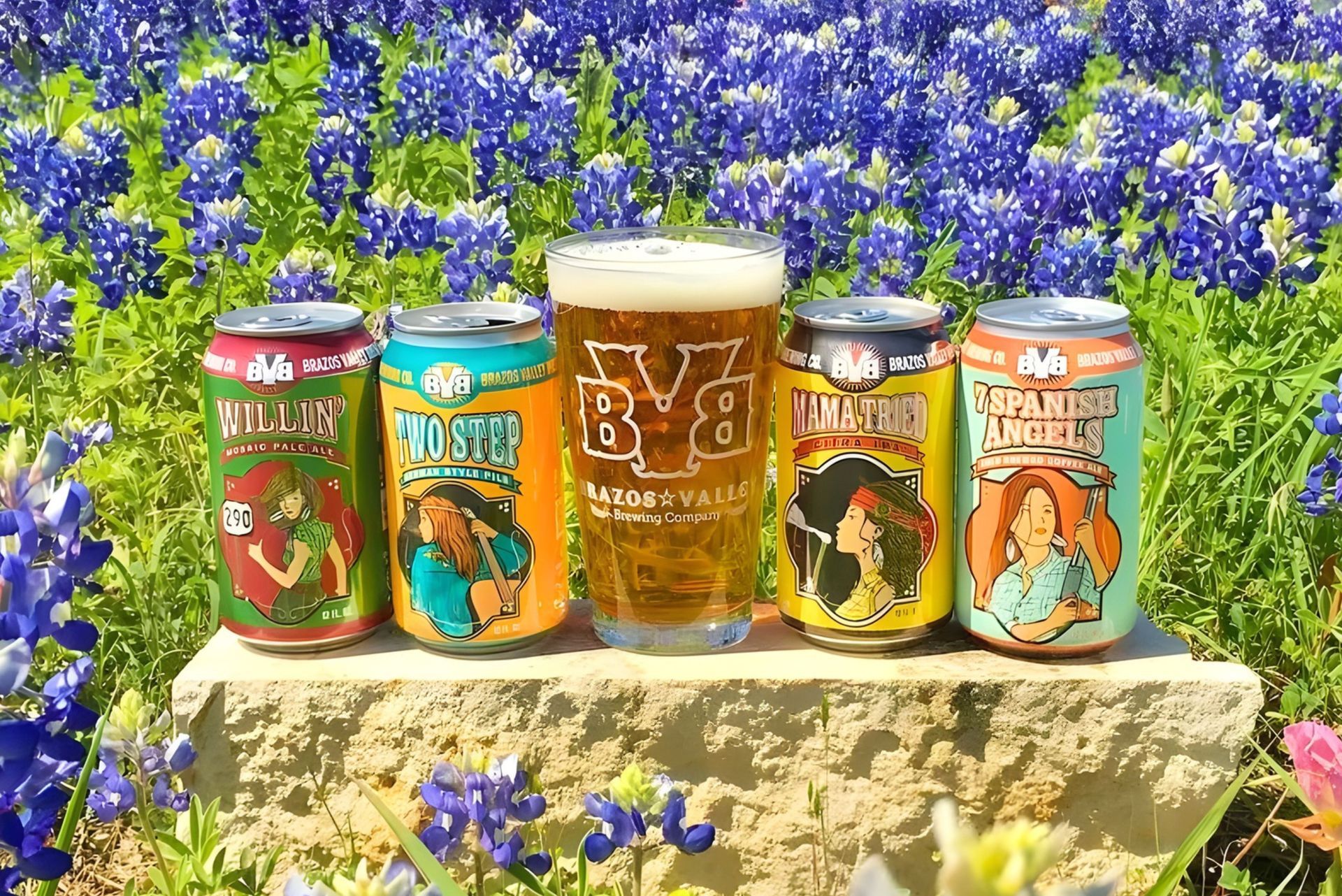Four cans and a glass of Blonde Giant beer on a stone ledge in a field of bluebonnets.