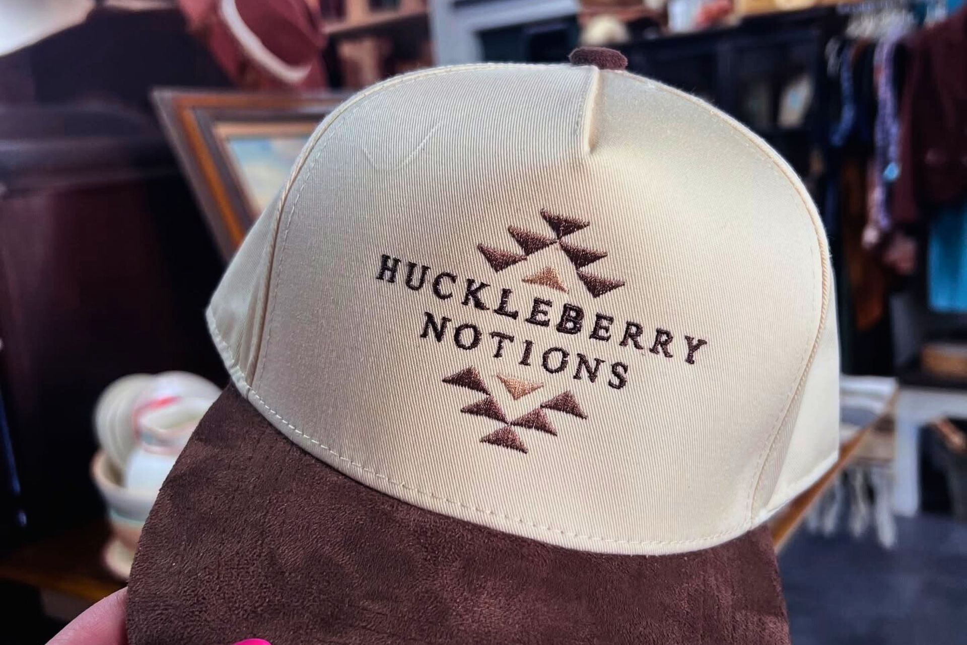 A cream-colored trucker hat with a brown suede brim and the embroidered text