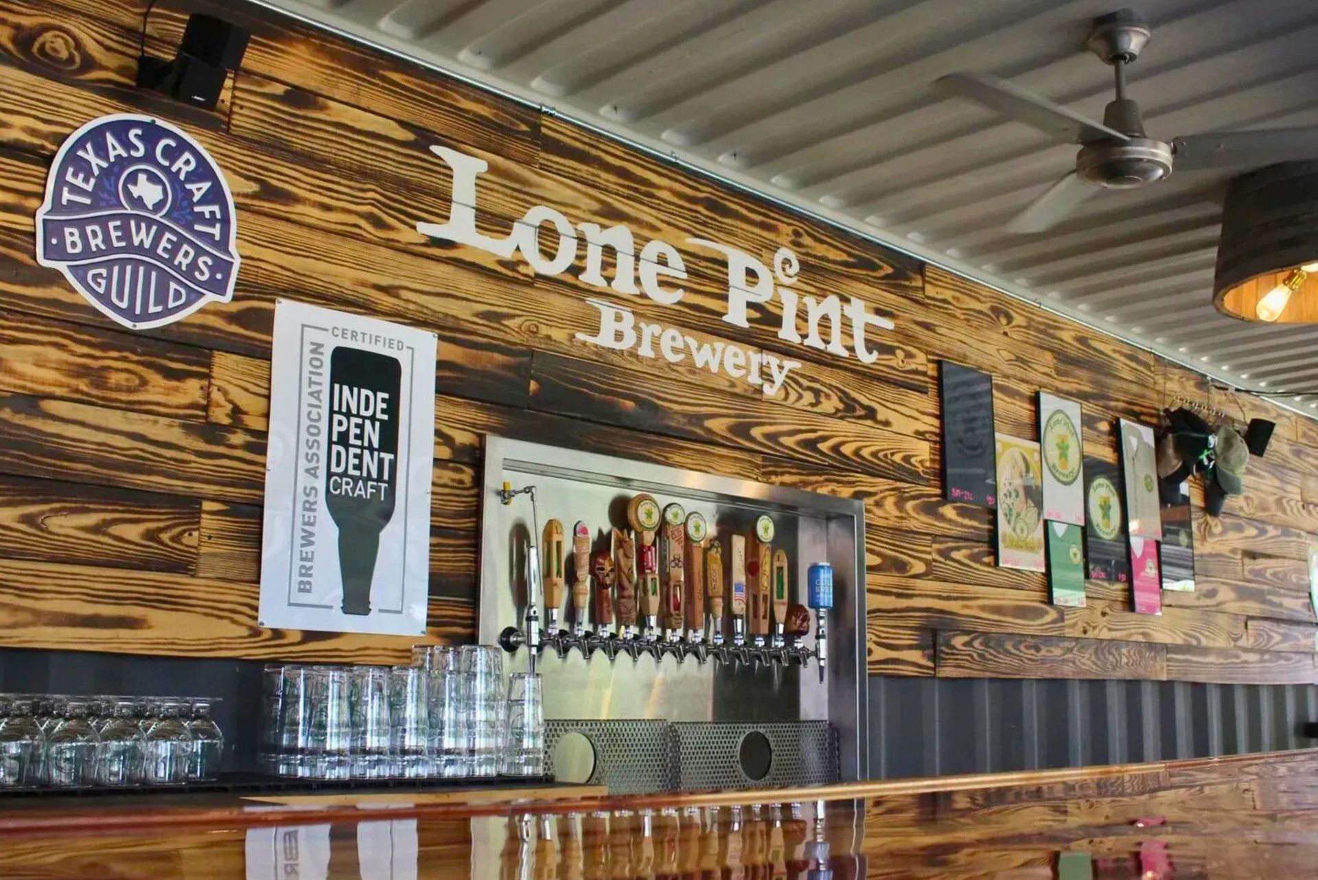 A bar counter with tap handles, glassware, and wooden walls featuring the Lone Pint Brewery logo and craft beer signage.