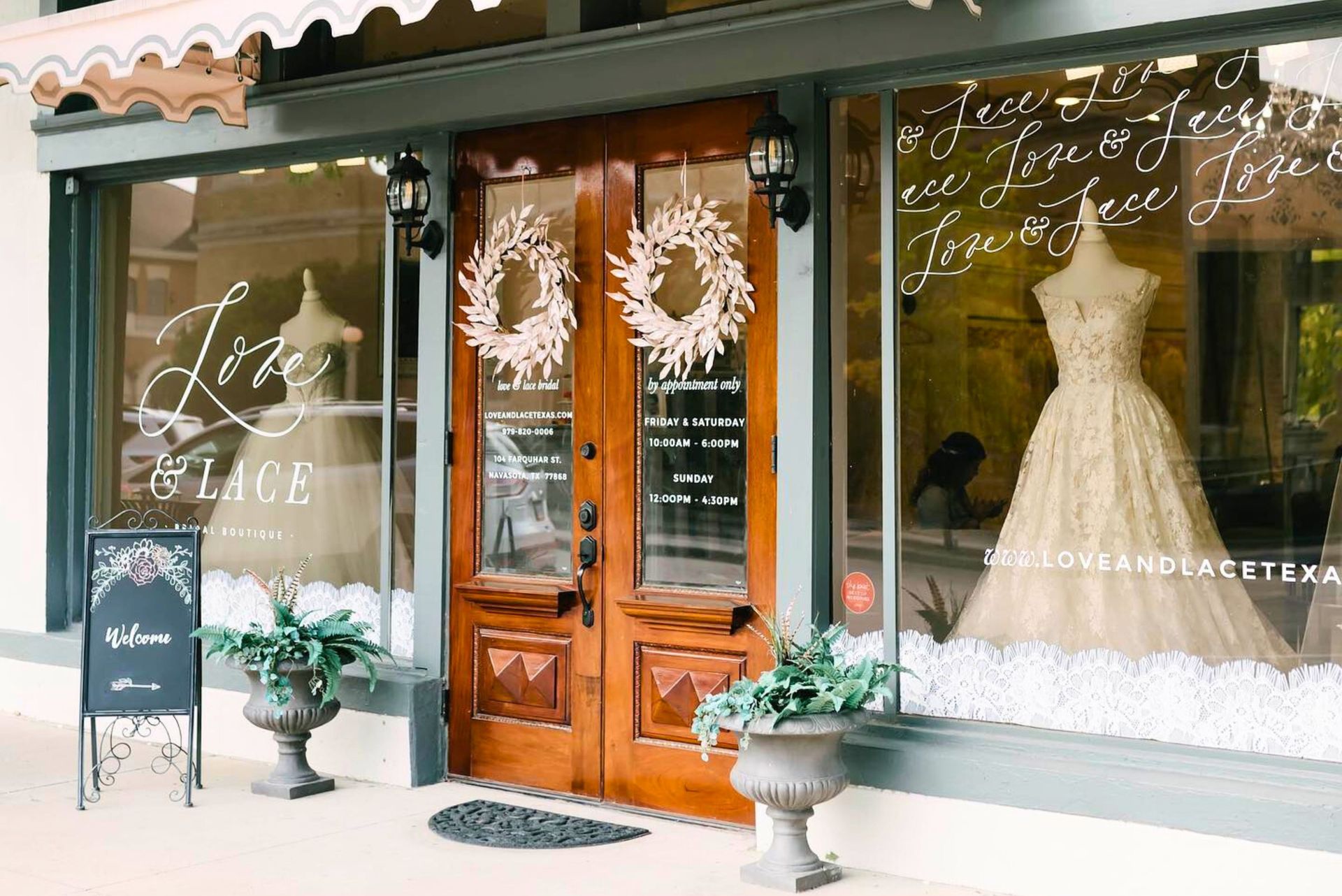 A bridal boutique storefront with a wooden double door, decorative wreaths, and mannequins wearing wedding gowns.