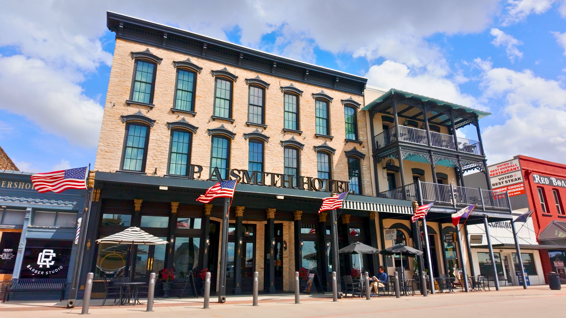 A three-story brick P.A. Smith Hotel building with a black balcony, lit against a deep blue dusk sky.