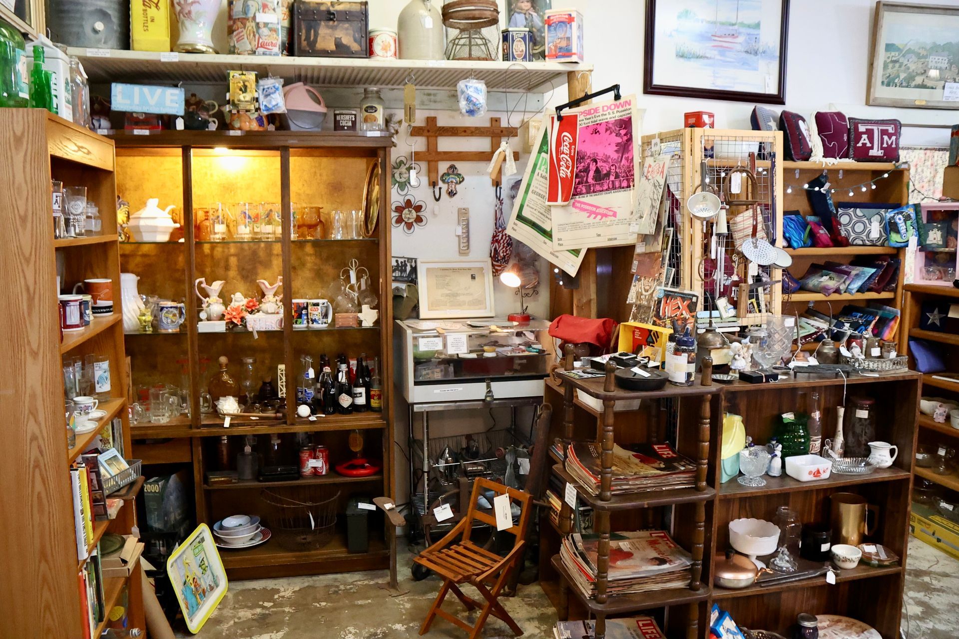 Antique shop interior filled with wooden shelves, display cabinets, glassware, home decor, and a small wooden chair.