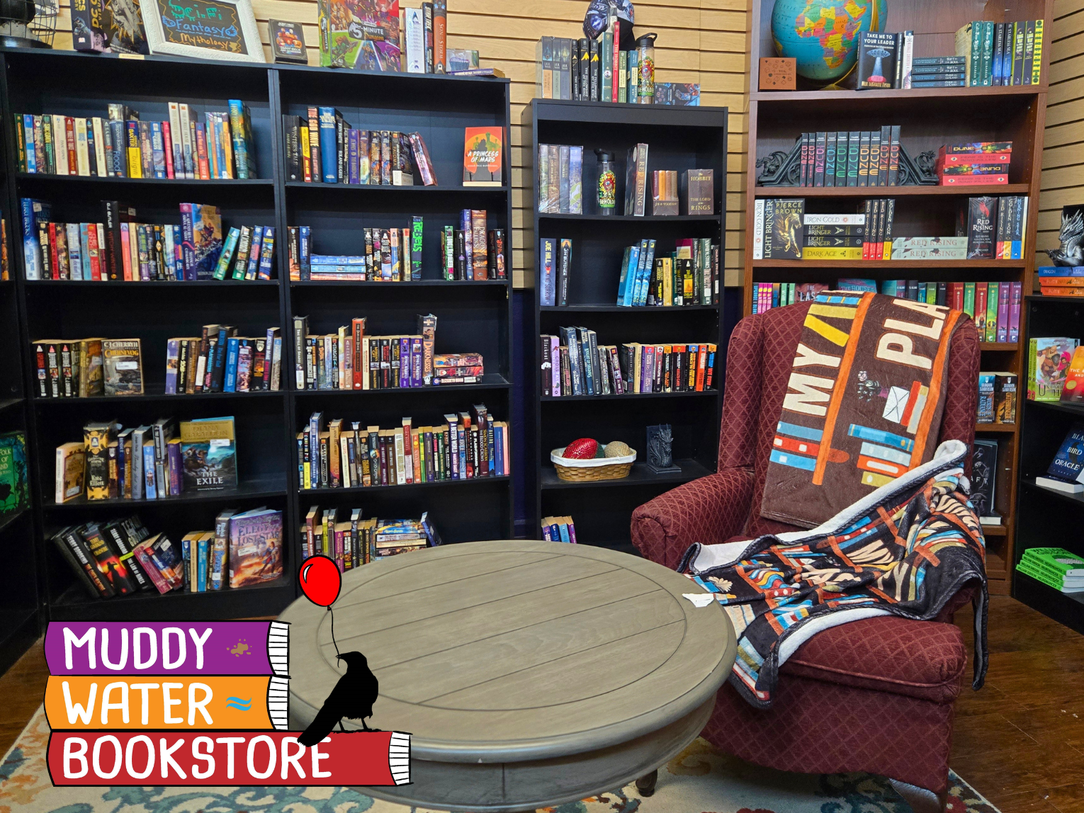 The storefront window of Muddy Water Bookstore features a sign with a bird and balloon, displaying new and used books.
