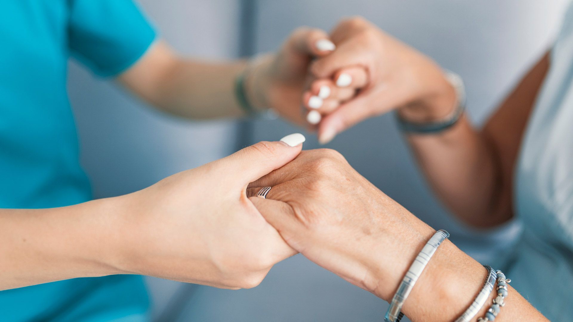 Nurse's hand holding a patient's hand for support, indoors, close-up.