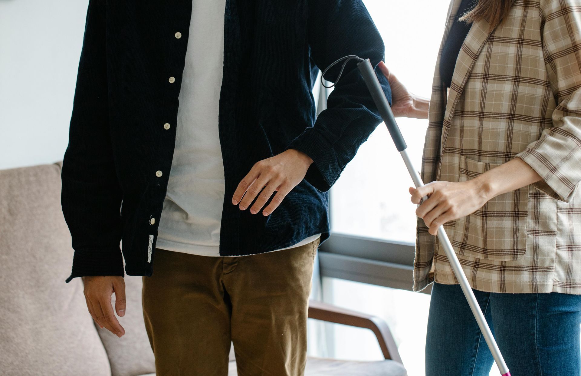 Person using a cane, guided by another person. Interior setting.