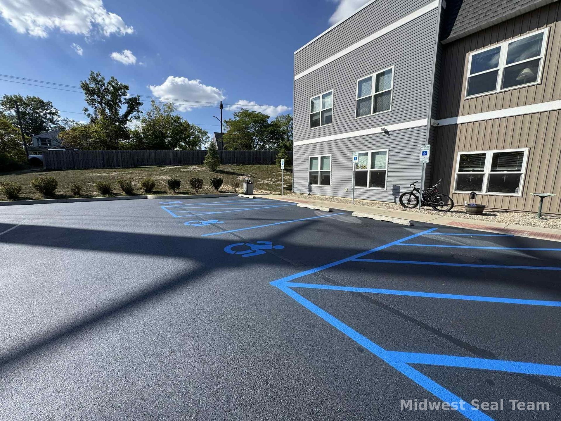 Image of Midwest Seal Team Sealcoating a parking lot in Fort Wayne, IN. You can see the Midwest Seal Team crew working on sealcoating the edges of the parking area. 