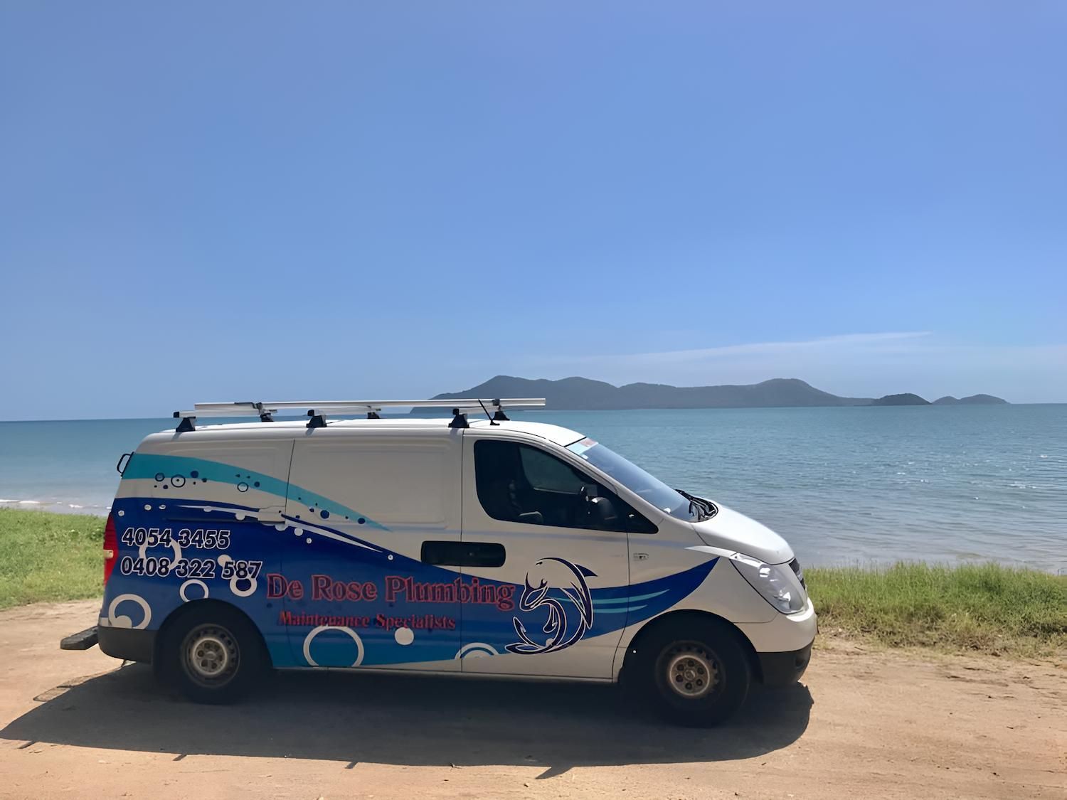 A White Van is Parked on the Beach Next to the Ocean — De Rose Plumbing In Bayview Heights, QLD