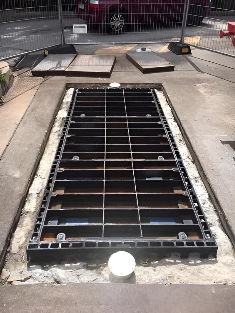A Manhole Cover is Sitting on the Ground Next to a Fence — De Rose Plumbing In Bayview Heights, QLD
