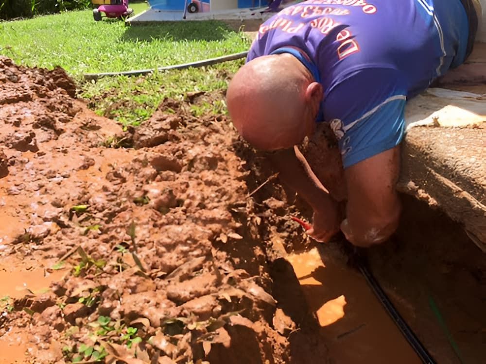 A Man in a Blue Shirt is Kneeling in the Mud — De Rose Plumbing In Bayview Heights, QLD
