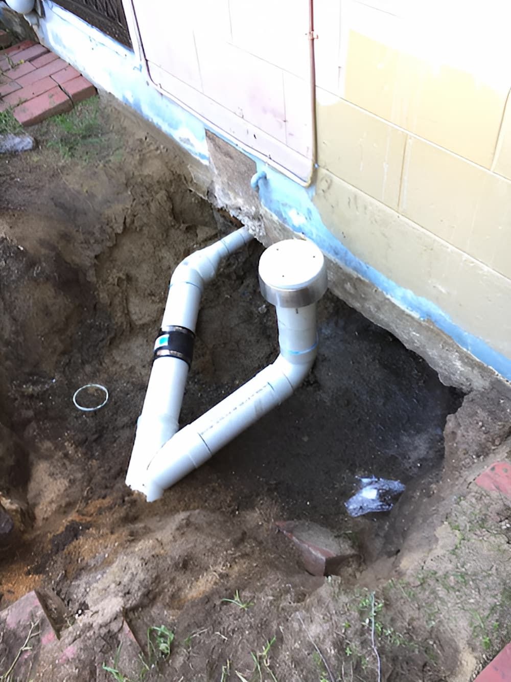 A White Pipe is Sitting in the Dirt Next to a House — De Rose Plumbing In Bayview Heights, QLD