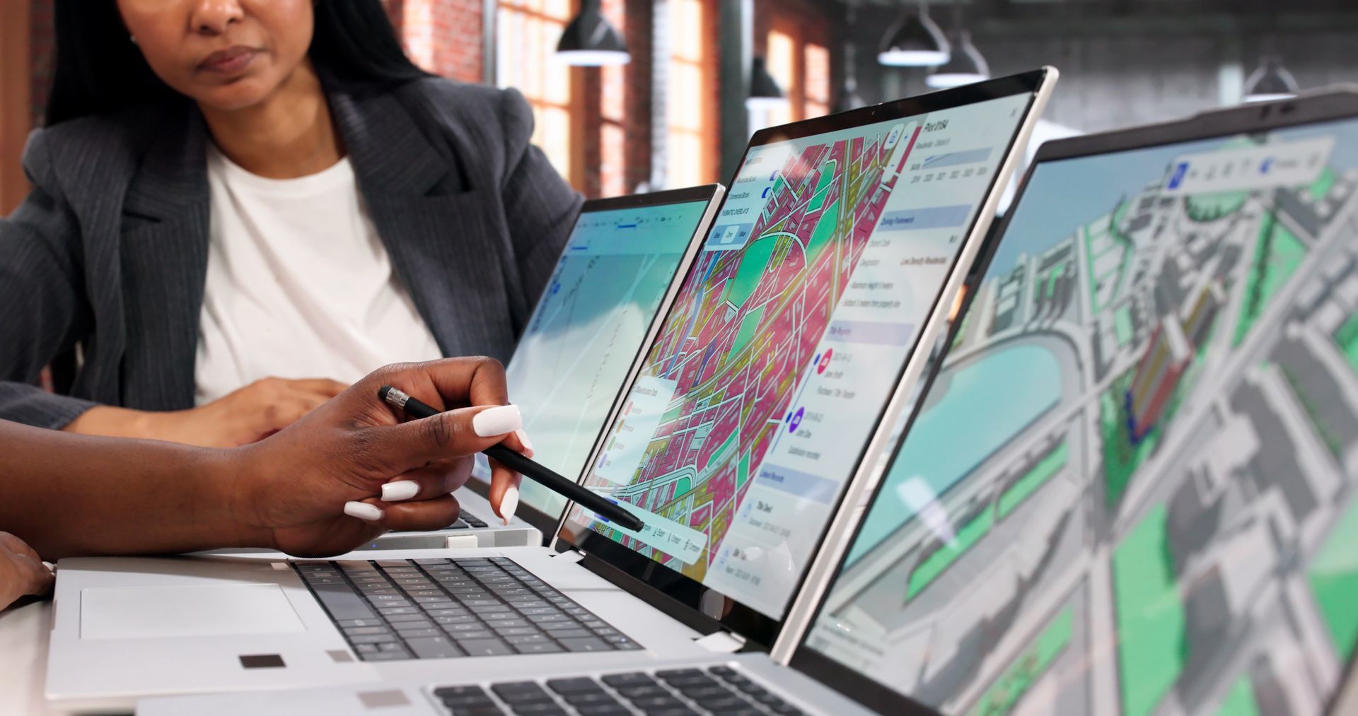 Person pointing at laptop screens showing maps and data in an office setting