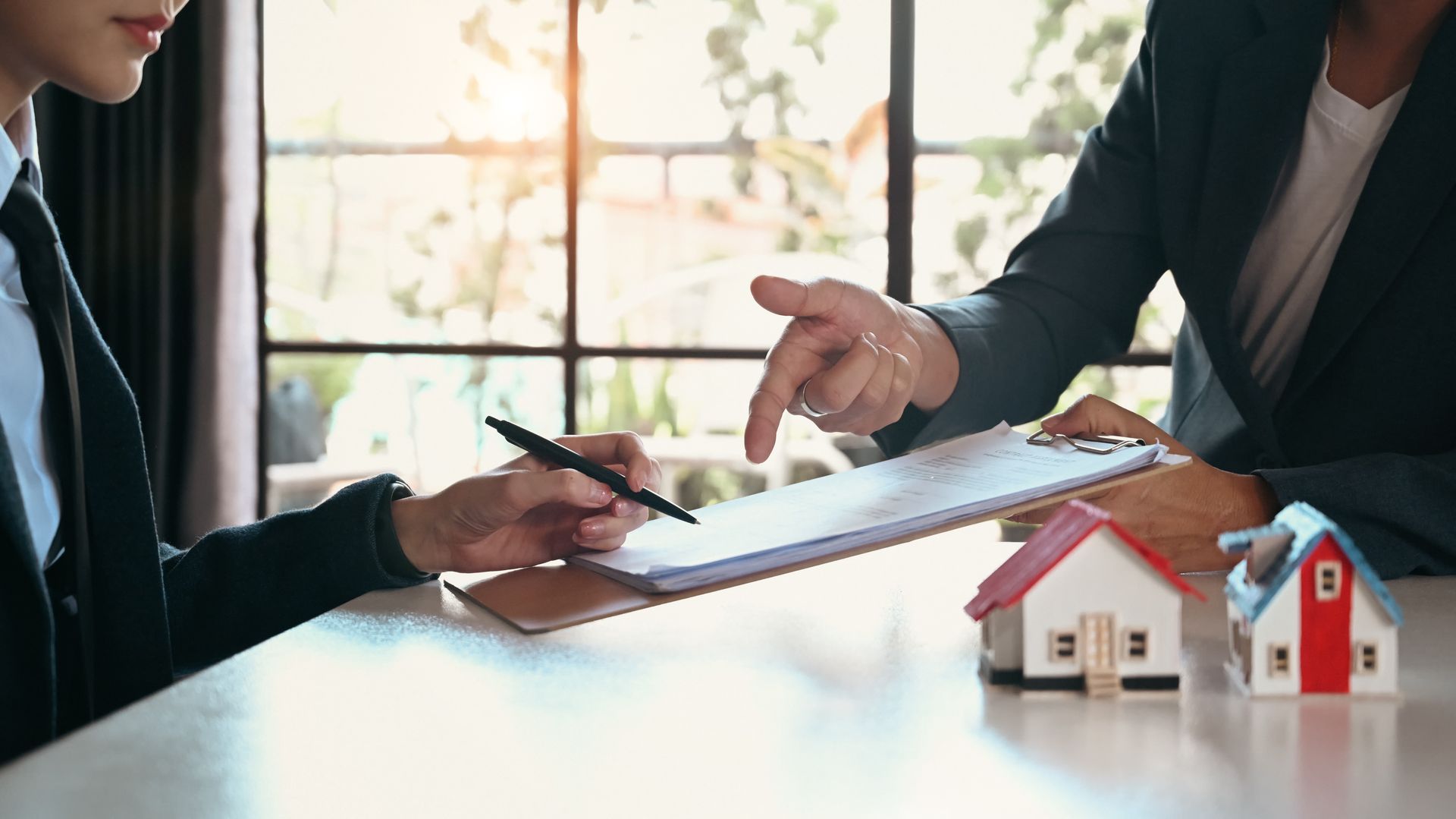 Two people reviewing real estate documents with a small house model on the table.