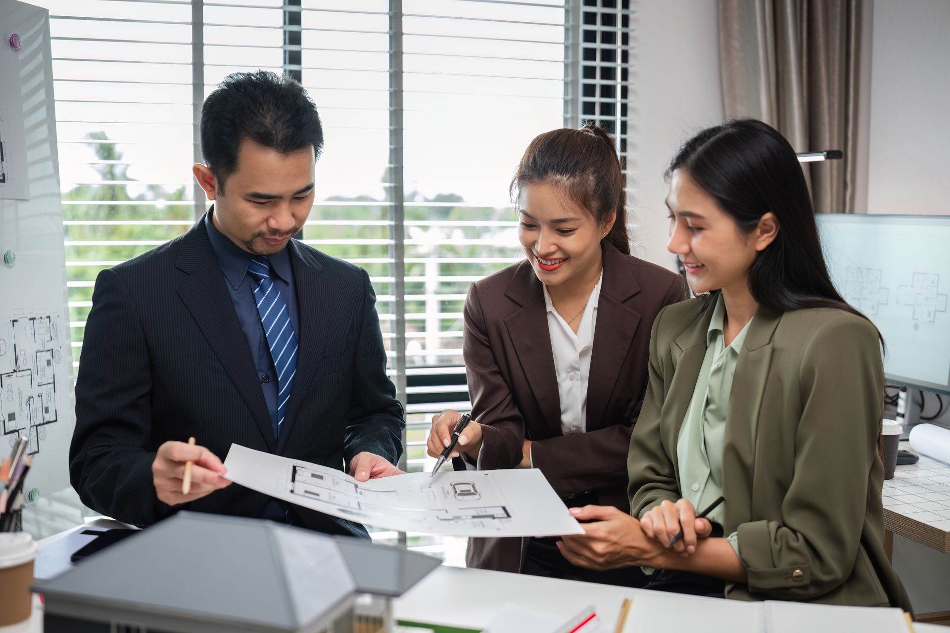 Three coworkers review documents at a desk in a bright office.