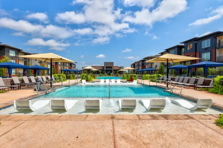 A large swimming pool surrounded by chairs and umbrellas in front of a building.