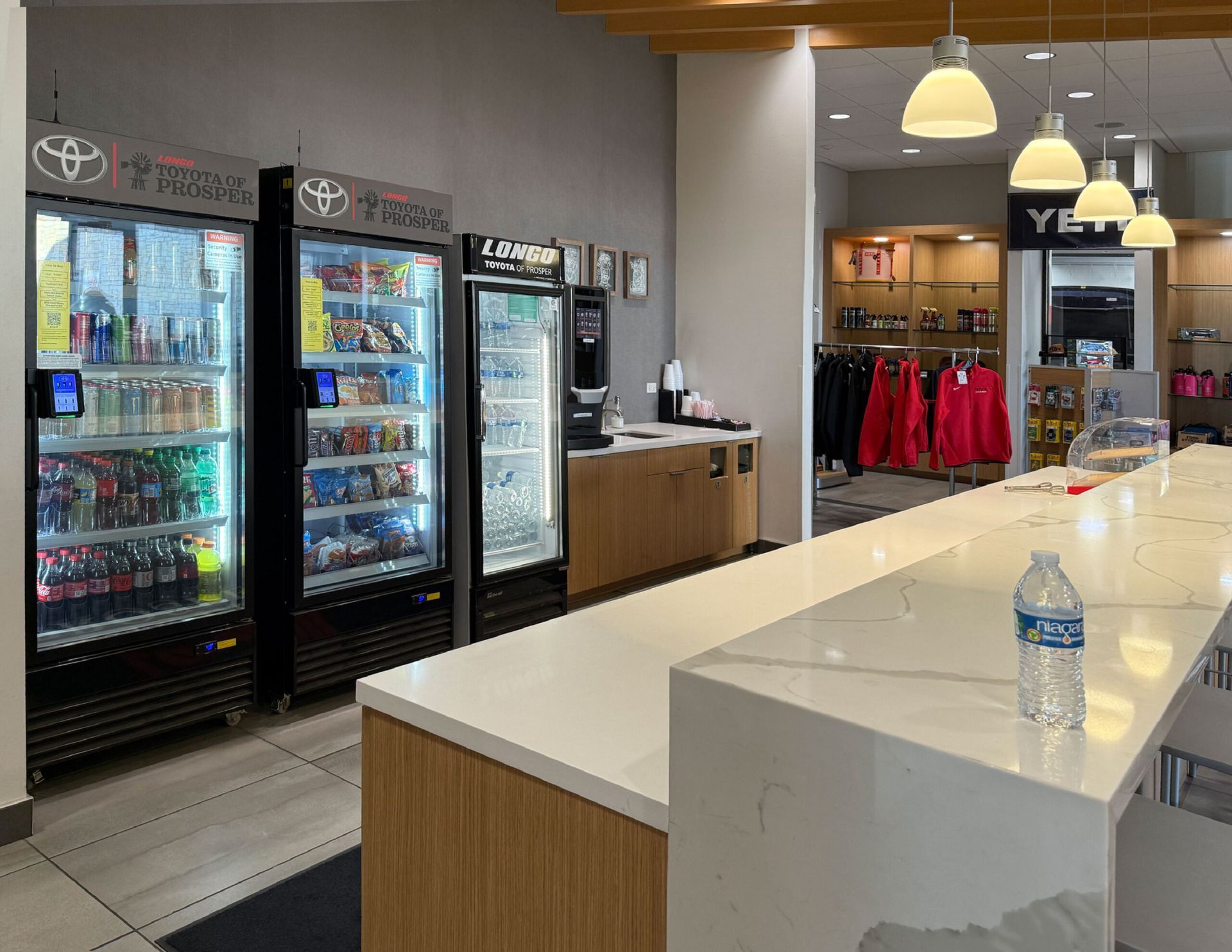 Convenience store counter with drink coolers, white island counter, and hanging lights