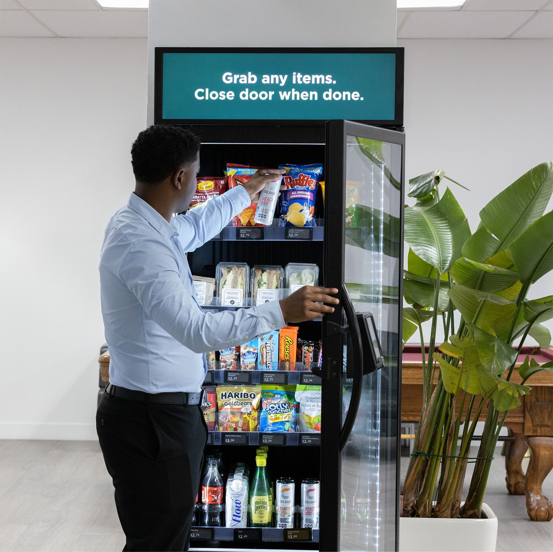 Man opening a vending machine stocked with snacks in a bright office lobby