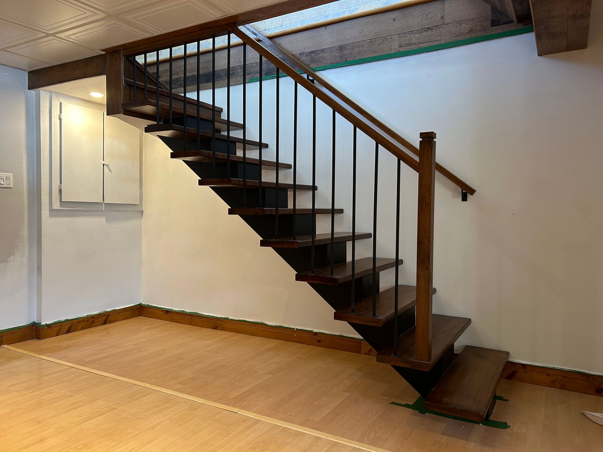 Escalier en bois avec rampes en métal noir, menant d'un sol en bois clair à un niveau supérieur.
