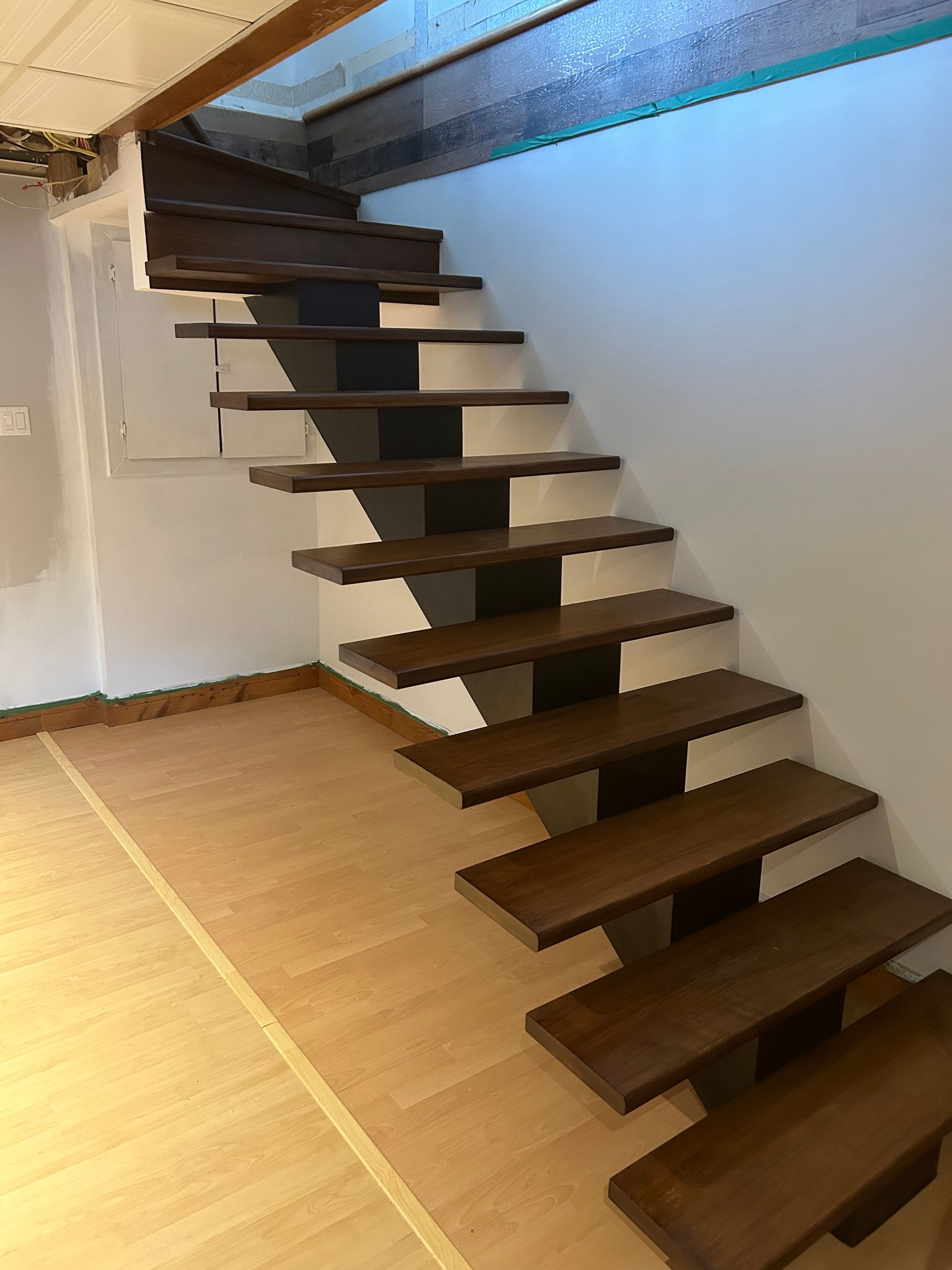 Escalier flottant en bois avec supports sombres sur un mur blanc et un parquet.