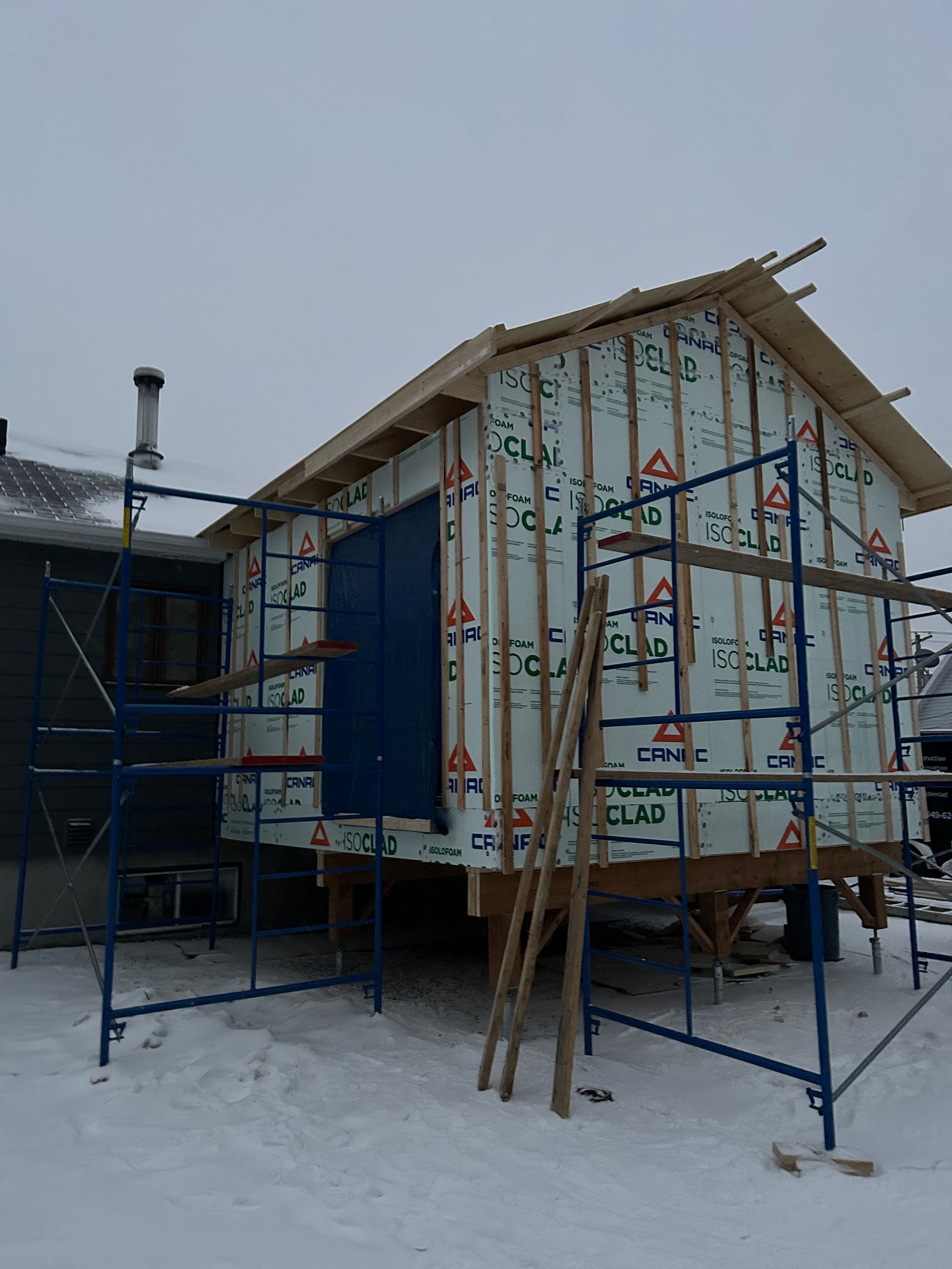 Construction d'un petit bâtiment, recouvert d'une bâche bleue, sur pilotis avec des échafaudages dans la neige.