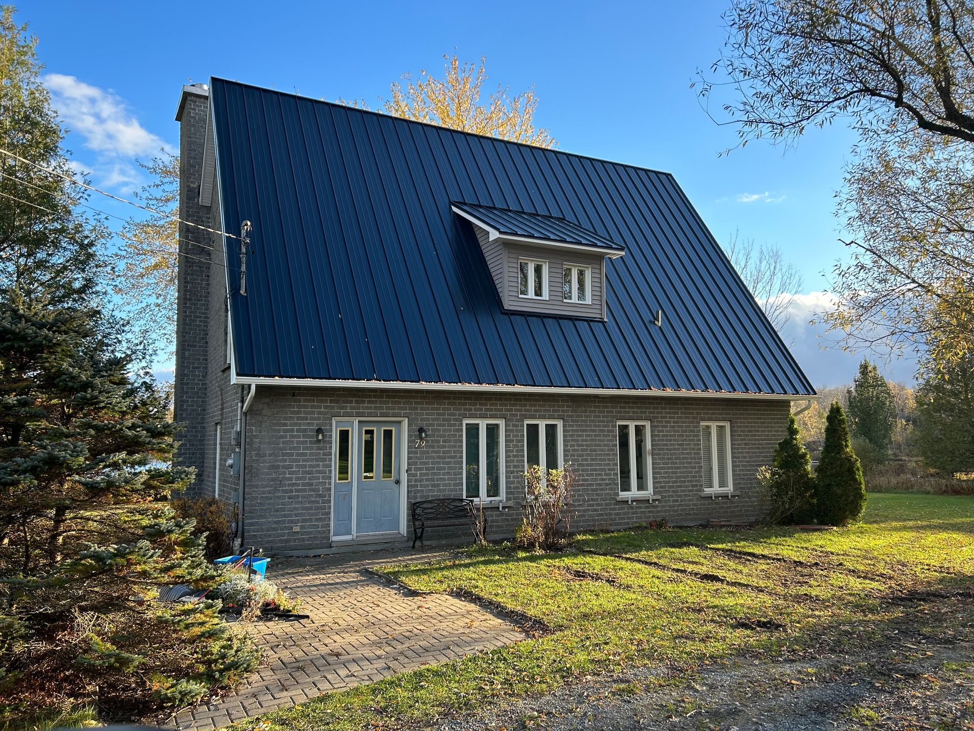 Maison en pierre au toit et à la cheminée bleus, située sur une pelouse ensoleillée.