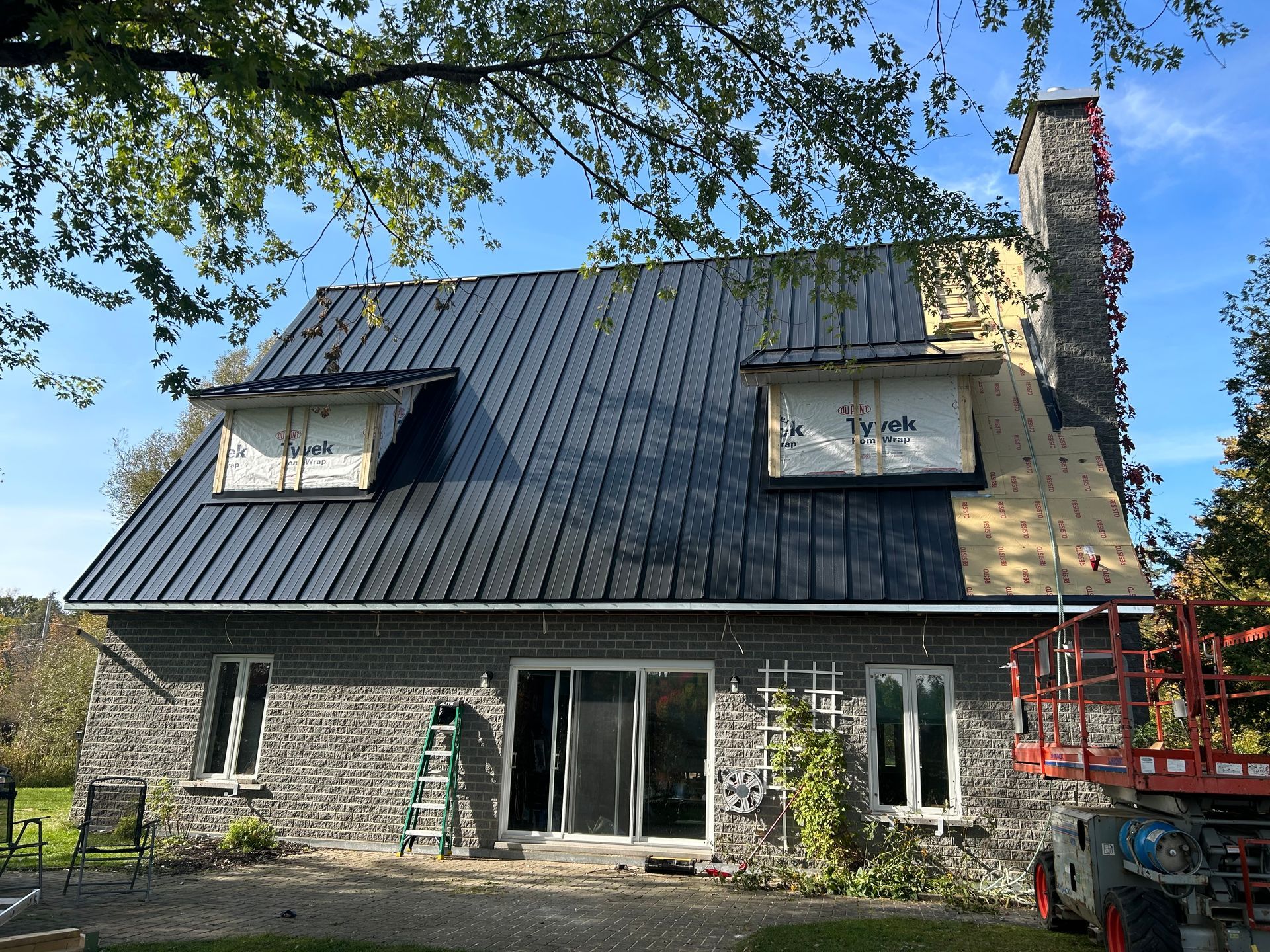 Maison en pierre avec toiture en métal noir en cours d'installation ; construction en cours.