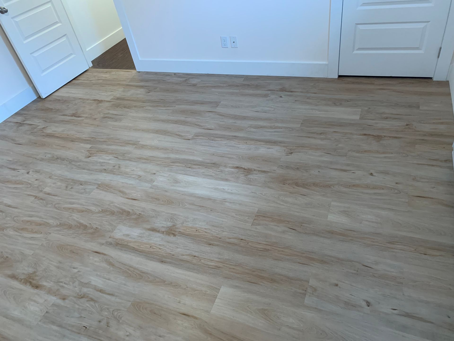 Un revêtement de sol clair imitant le bois habille la pièce, jouxtant des plinthes et des portes blanches.