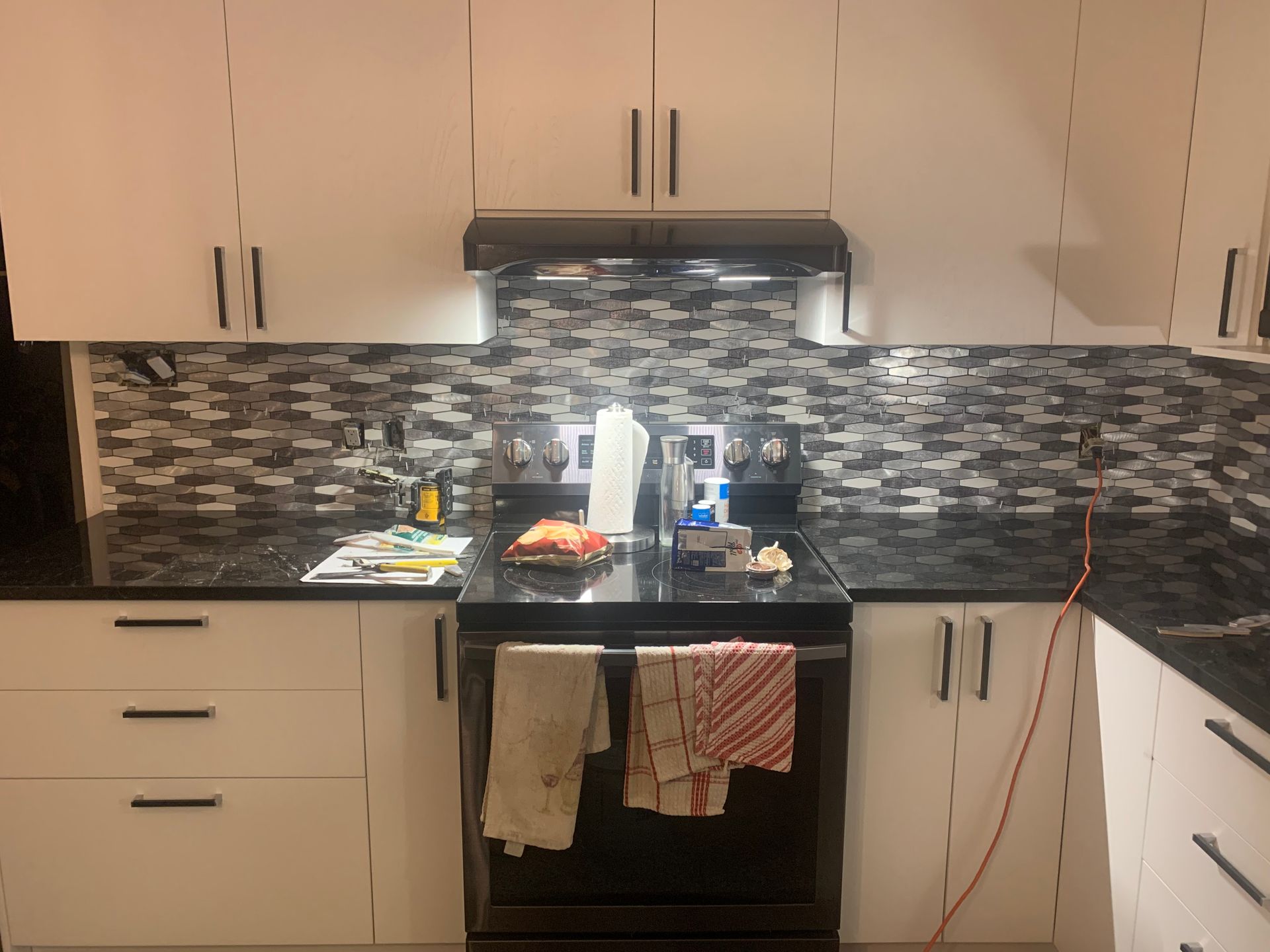 Cuisine avec placards blancs, comptoirs et crédence noirs, cuisinière au centre avec des torchons.