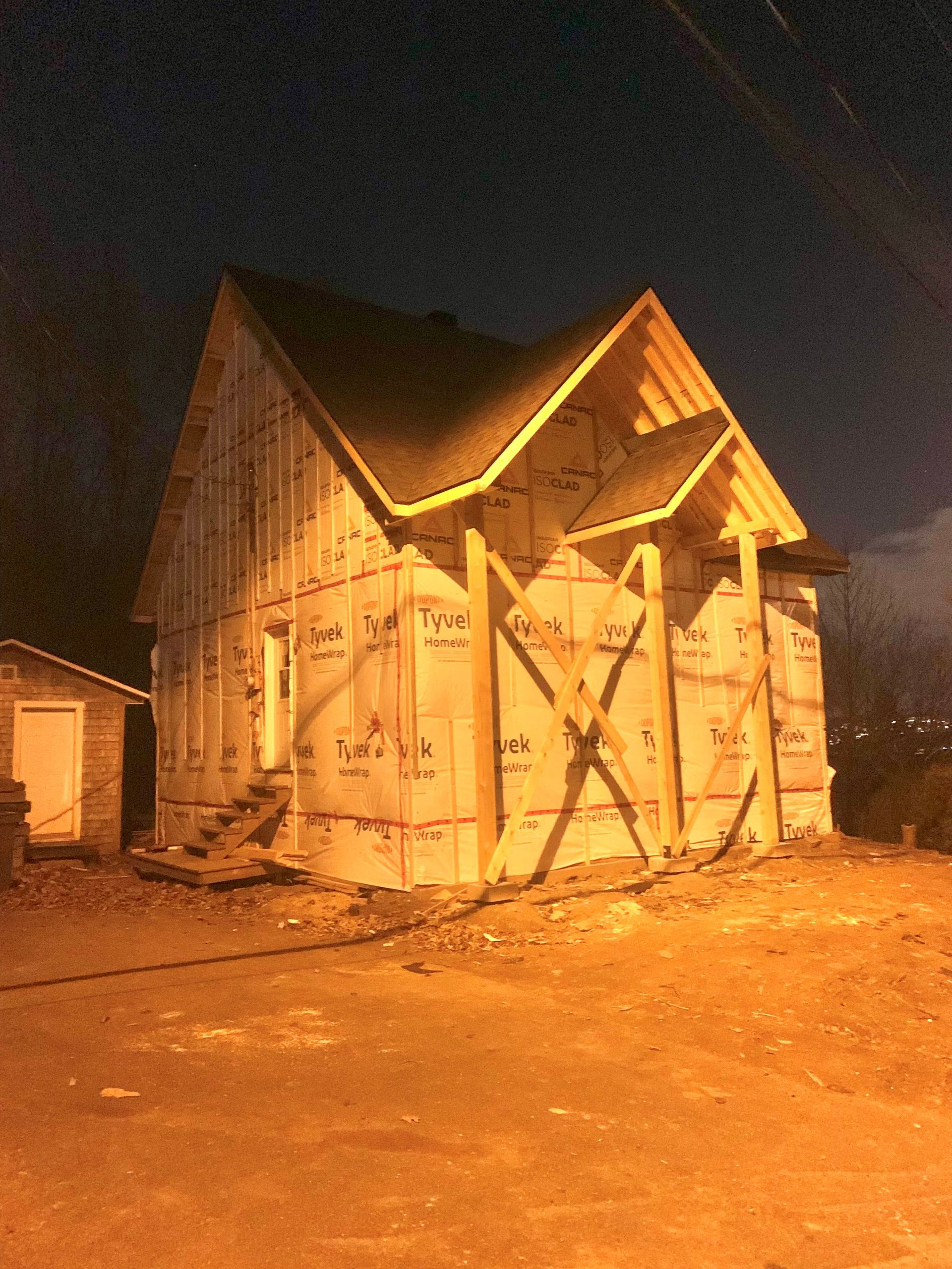 Construction d'une maison de nuit, ossature en contreplaqué, revêtement et contreventement. Ciel sombre.